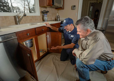 Uniformed plumber speaking with a customer about garbage disposal repairs and looking under their kitchen sink