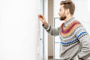 Man wearing a sweater adjusting the thermostat