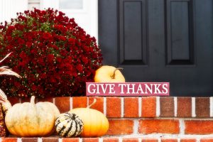 Small pumpkins, potted flowers, and give thanks sign on brick steps