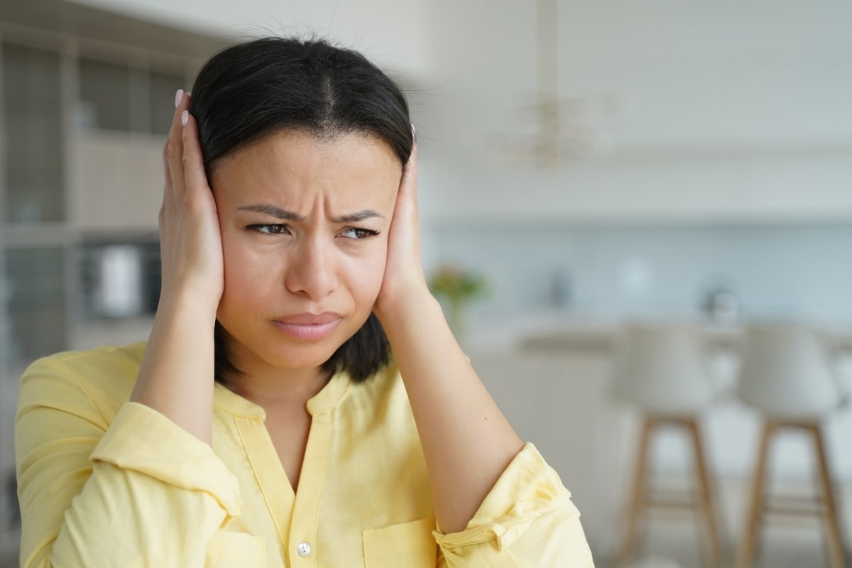 Woman in yellow shirt covering her ears