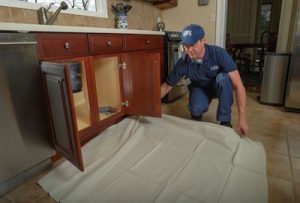 Plumber laying tarp under kitchen sink before repair.