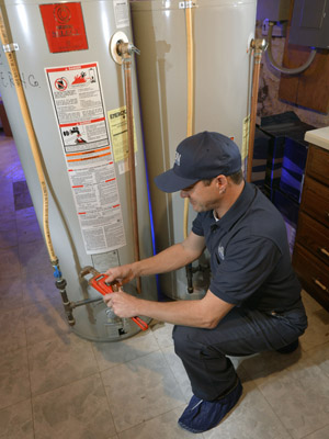 Len The Plumber technician kneeling and preparing to make water heater repairs in a DMV Metro home.