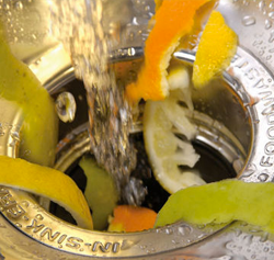 citrus peels going down a garbage disposal with running water