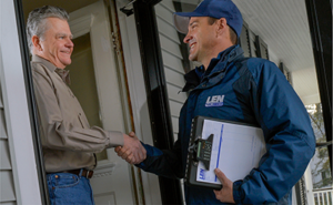 Len The Plumber technician smiling and shaking a customer's hand in a doorway.